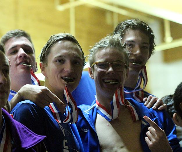 Junior Braxton Flowers, sophomore Riley OHara and seniors Sam Schorr and Damian Wilkerson bite their first place medals after winning the 200m medley relay.