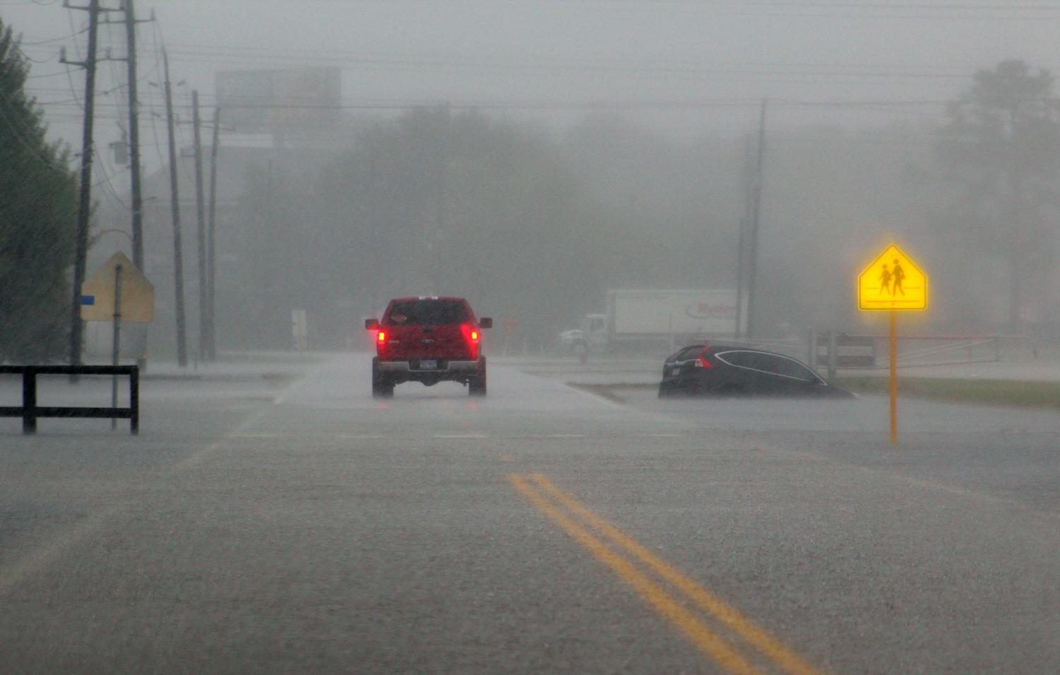 A car drives through the rain while the street floods.

