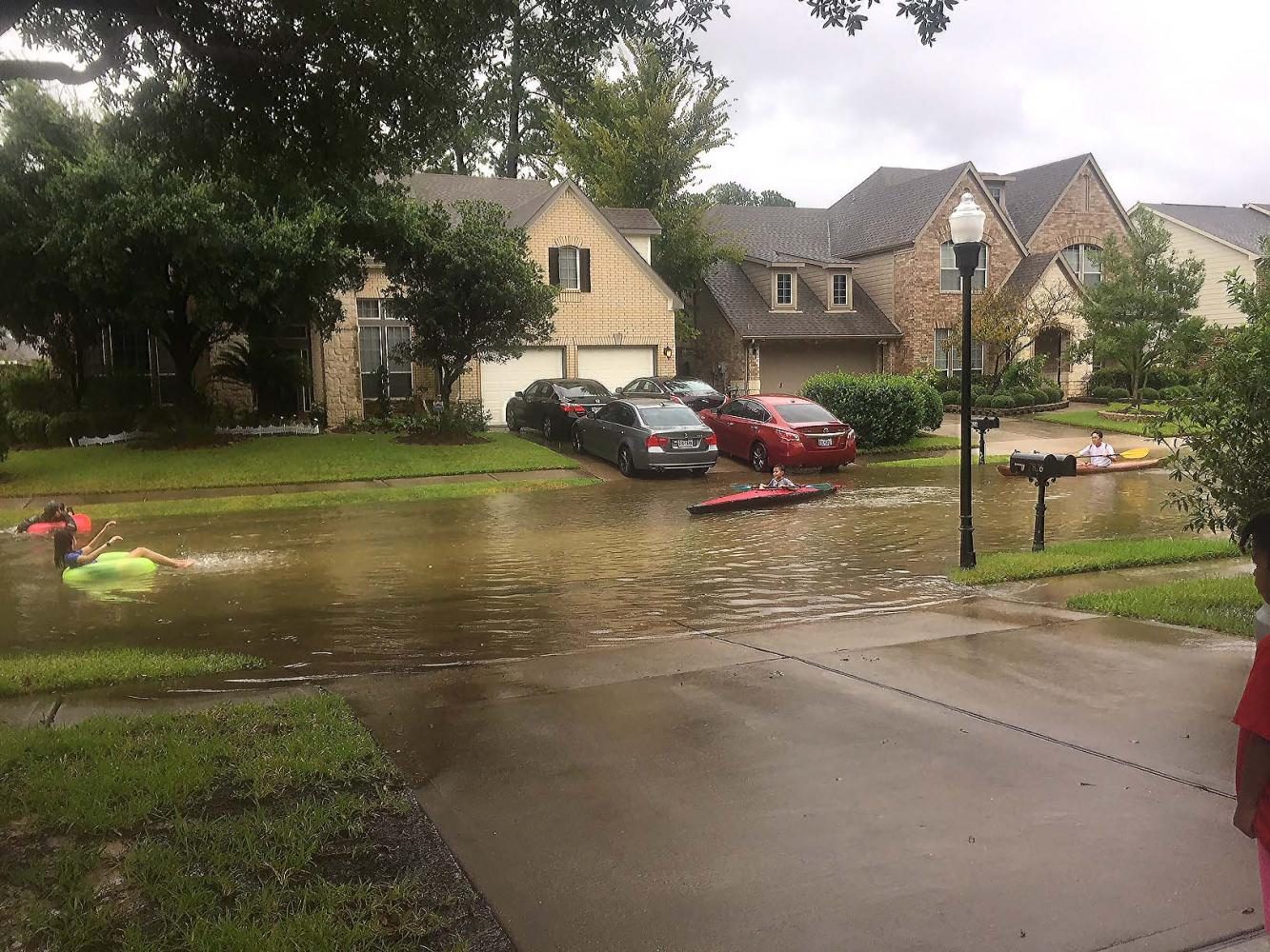 People in inner tubes and canoes float down a flooded street.
