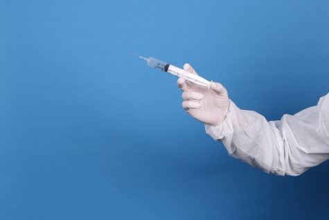 Doctor in protective suit and face mask holding syringe by focusonmore.com is licensed under CC BY 2.0